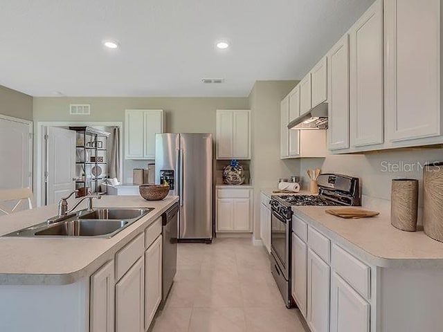 kitchen featuring appliances with stainless steel finishes, white cabinets, light tile patterned floors, a center island with sink, and sink