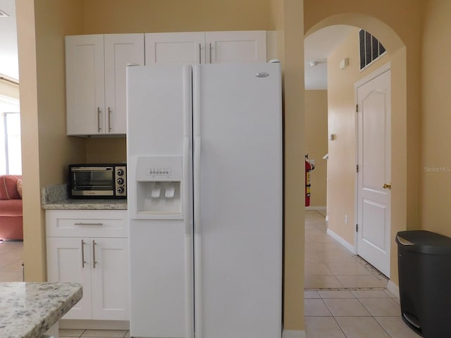 kitchen with light stone counters, light tile patterned floors, white fridge with ice dispenser, and white cabinets