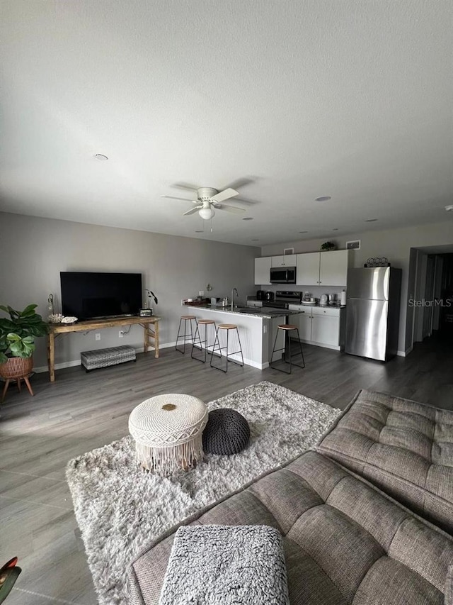 living room featuring wood-type flooring, a textured ceiling, sink, and ceiling fan