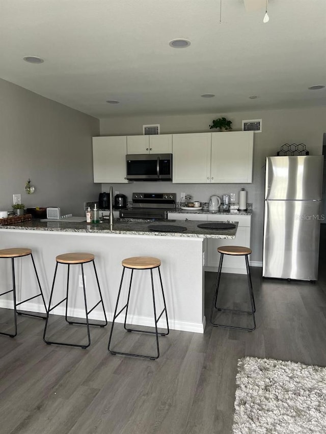 kitchen with appliances with stainless steel finishes, a kitchen breakfast bar, wood-type flooring, and white cabinetry