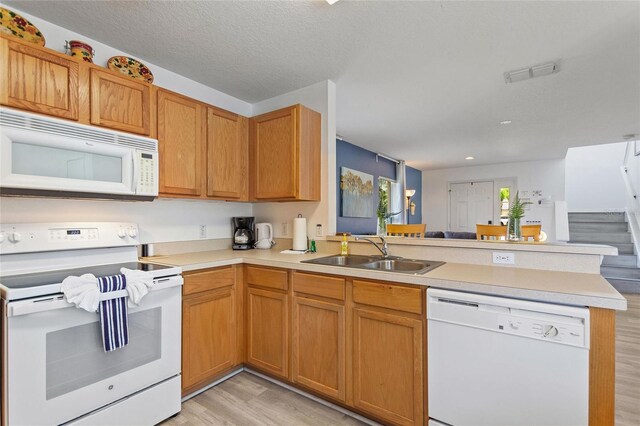 kitchen featuring sink, white appliances, light wood-type flooring, and kitchen peninsula