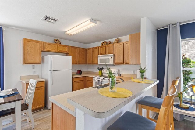 kitchen featuring a kitchen breakfast bar, light hardwood / wood-style flooring, white appliances, and kitchen peninsula