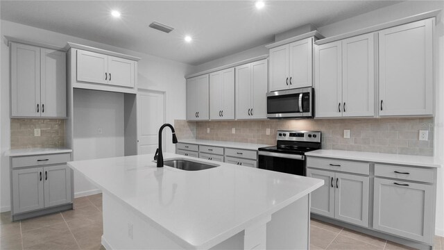 kitchen featuring light tile patterned flooring, stainless steel appliances, backsplash, and a center island with sink