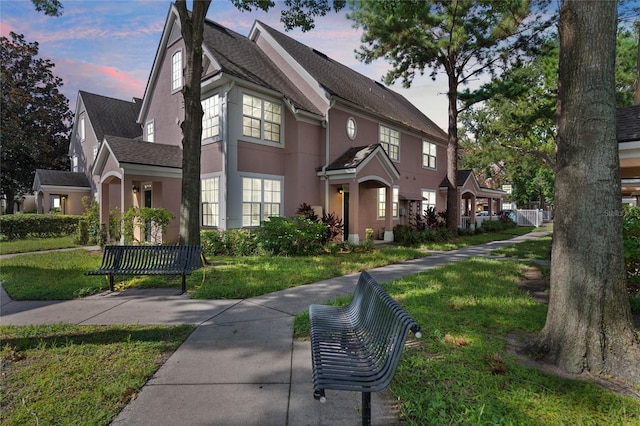 view of front of property with a yard, a shingled roof, and stucco siding