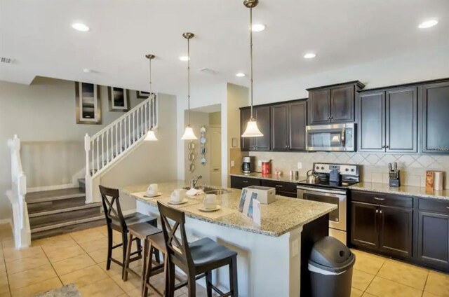 kitchen with light tile patterned flooring, sink, appliances with stainless steel finishes, and an island with sink