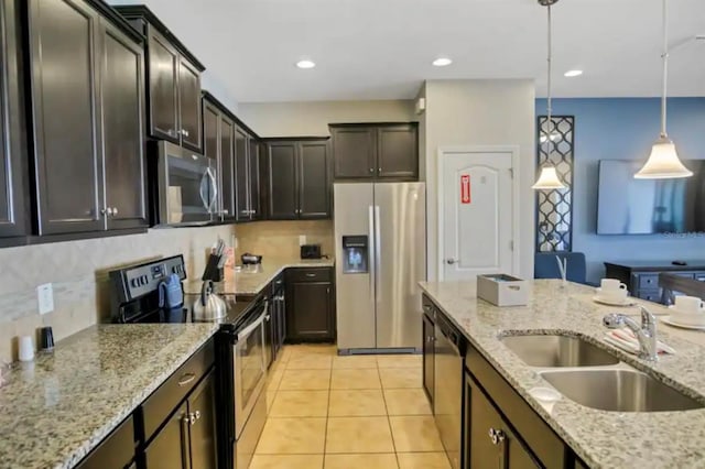 kitchen with stainless steel appliances, a sink, hanging light fixtures, dark brown cabinets, and light stone countertops