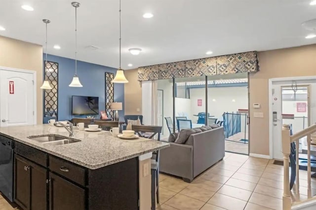 kitchen with open floor plan, hanging light fixtures, light stone countertops, a kitchen island with sink, and a sink