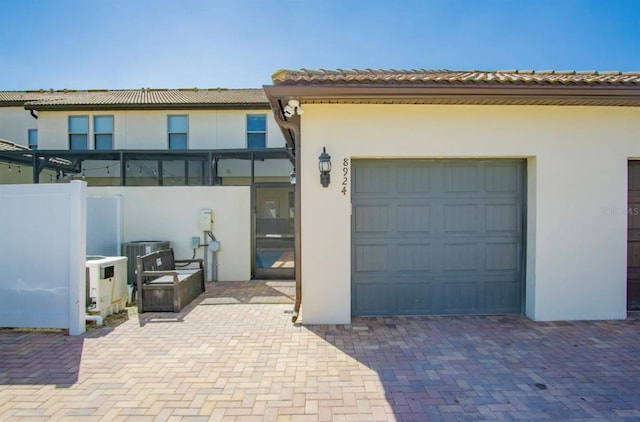 exterior space with decorative driveway, an attached garage, cooling unit, and stucco siding