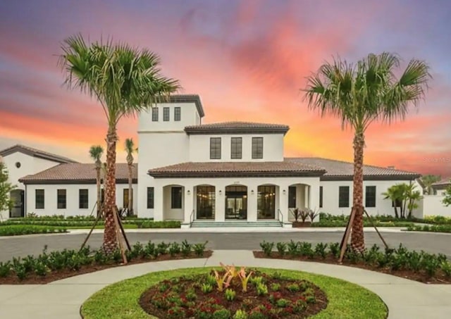 back of house at dusk featuring curved driveway and stucco siding