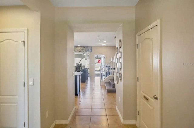 hall featuring light tile patterned floors, baseboards, and stairway