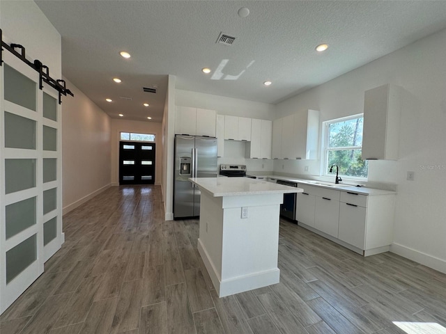 kitchen with a barn door, visible vents, appliances with stainless steel finishes, a center island, and white cabinetry