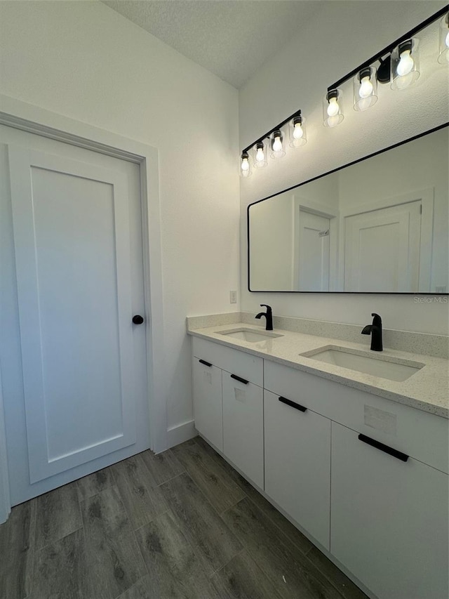 bathroom featuring double vanity, a textured ceiling, a sink, and wood finished floors