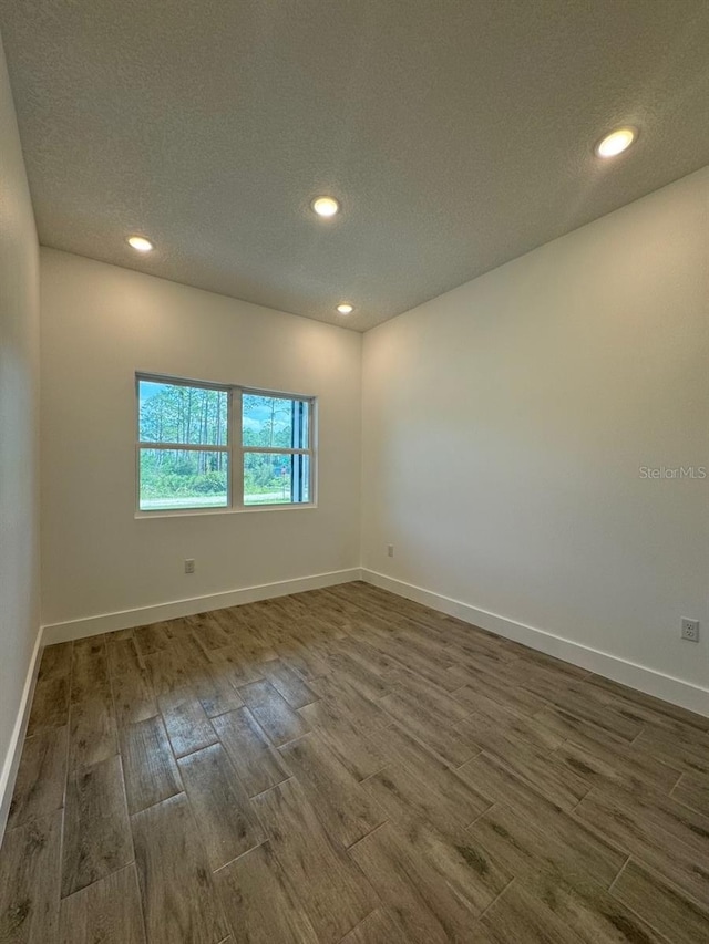 spare room featuring dark wood-style floors, a textured ceiling, recessed lighting, and baseboards