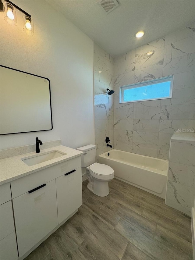 bathroom with visible vents, toilet, vanity, wood finished floors, and  shower combination