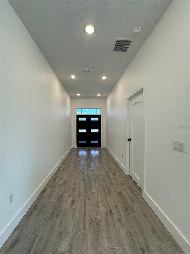 hall featuring dark wood-style flooring, visible vents, a textured ceiling, and baseboards