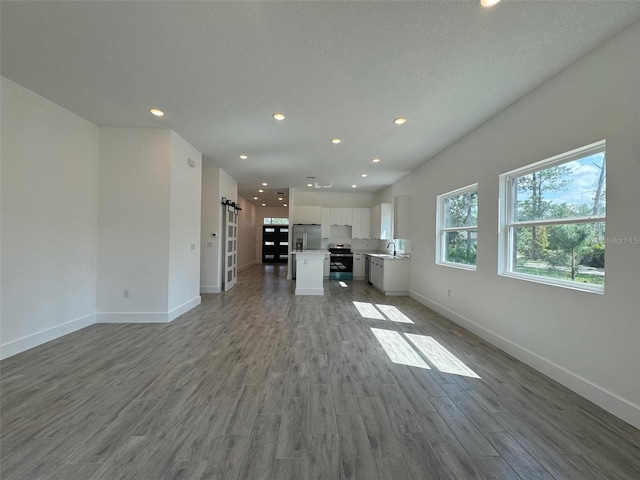 unfurnished living room with wood finished floors, baseboards, and a barn door