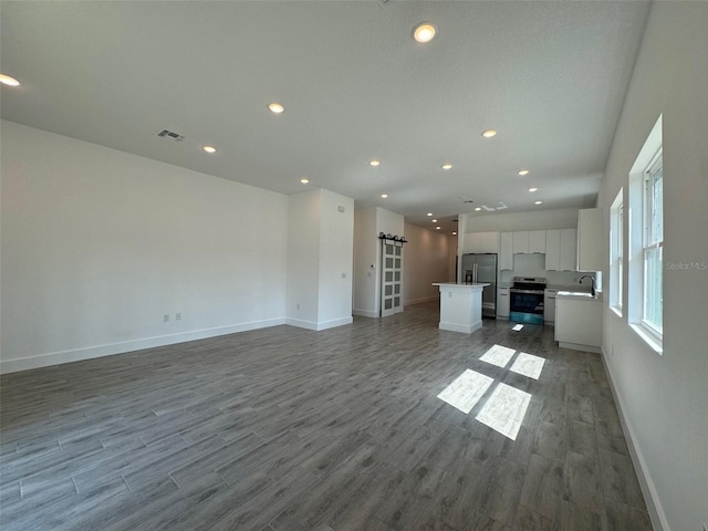 unfurnished living room with visible vents, a barn door, a sink, wood finished floors, and baseboards