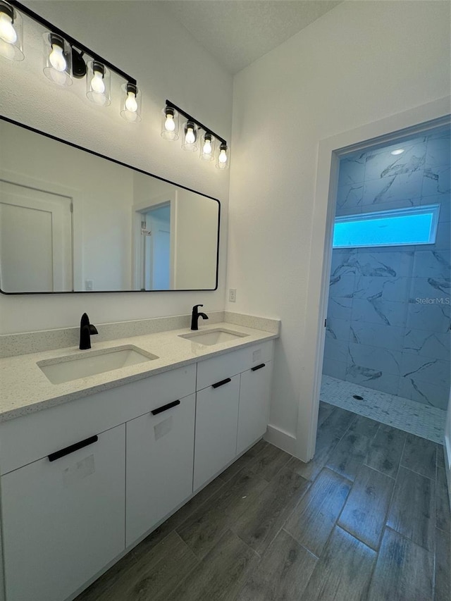 bathroom with wood finish floors, a sink, a marble finish shower, and double vanity