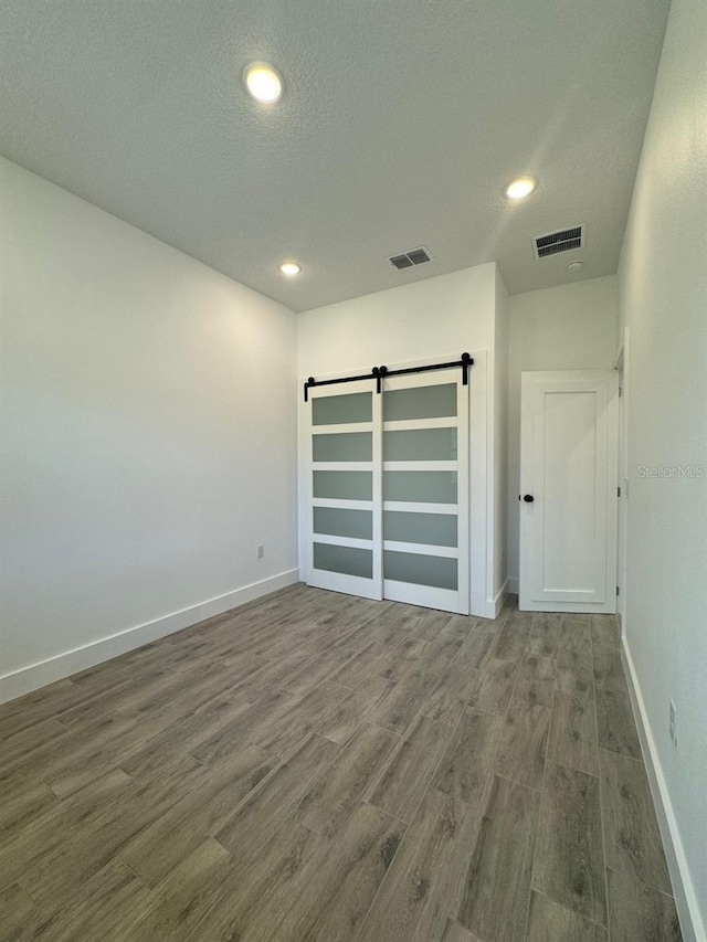 unfurnished room with a barn door, visible vents, baseboards, and wood finished floors