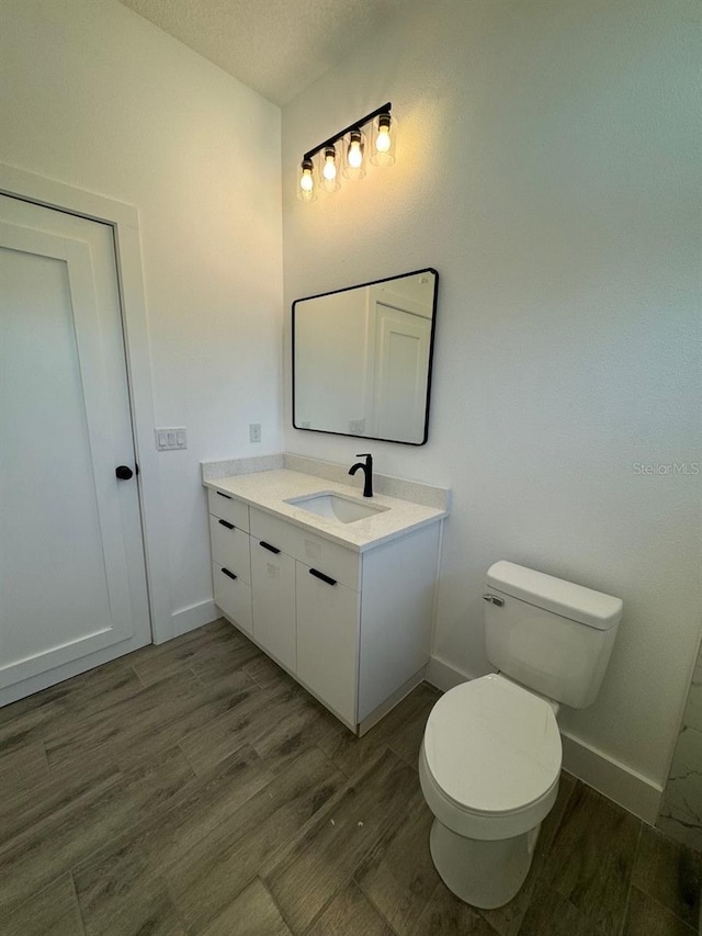 half bath featuring baseboards, toilet, wood finished floors, a textured ceiling, and vanity