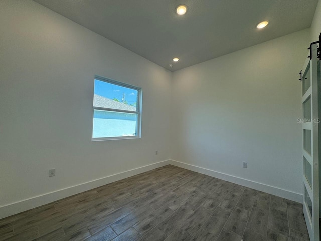 empty room with a barn door, recessed lighting, dark wood finished floors, and baseboards