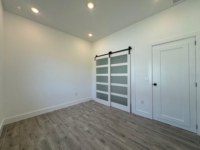 unfurnished bedroom featuring recessed lighting, wood finished floors, baseboards, and a barn door