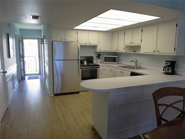 kitchen with stainless steel appliances, a peninsula, a sink, visible vents, and light wood-style floors