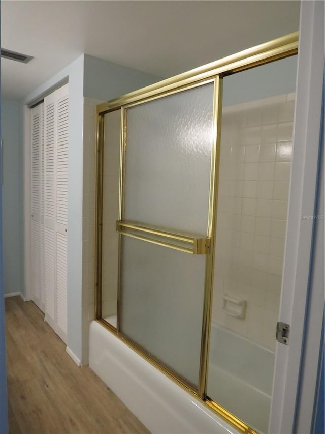 bathroom with visible vents, bath / shower combo with glass door, and wood finished floors