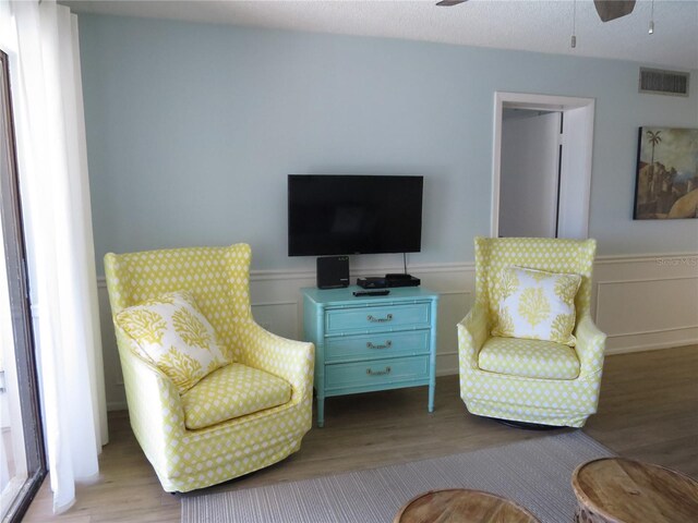 living area featuring a ceiling fan, wainscoting, visible vents, and wood finished floors