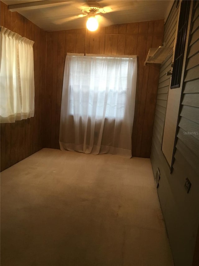 carpeted spare room featuring wood walls and ceiling fan