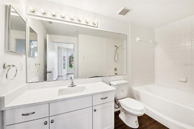 full bathroom with a textured ceiling, toilet, vanity, tiled shower / bath combo, and hardwood / wood-style floors