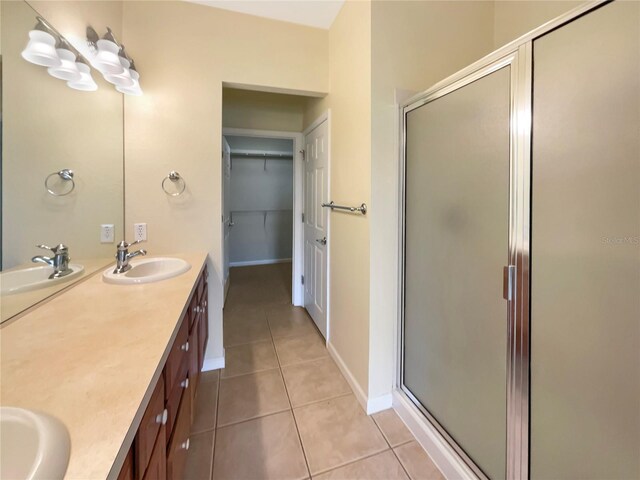 bathroom with tile patterned floors, a shower with door, and dual bowl vanity