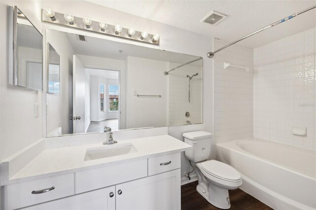 full bathroom featuring tiled shower / bath, a textured ceiling, toilet, vanity, and wood-type flooring