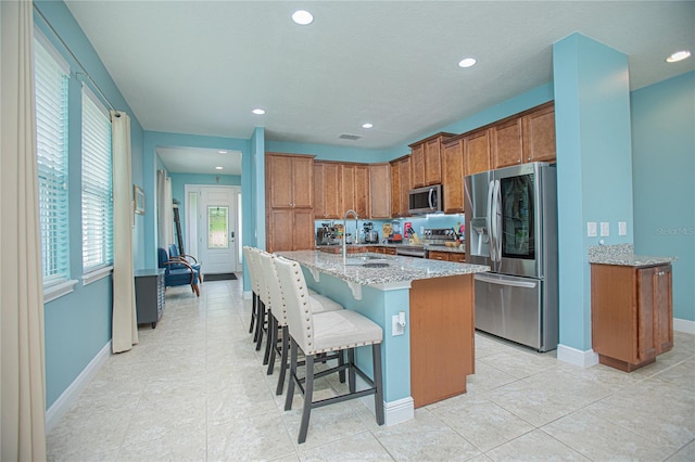 kitchen with light tile patterned flooring, sink, stainless steel appliances, and an island with sink