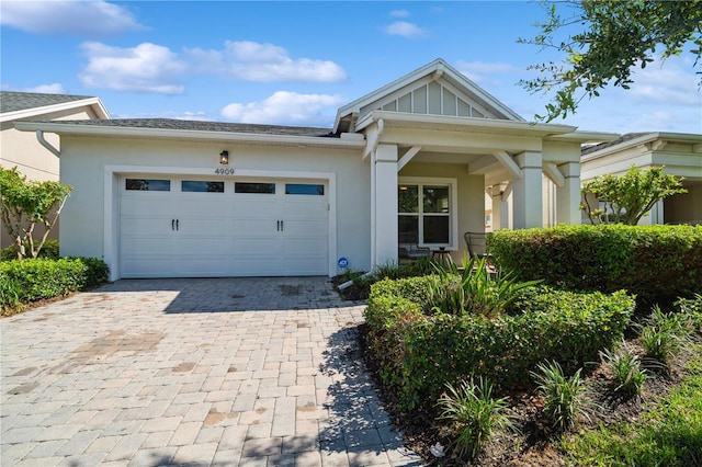 view of front of home featuring board and batten siding, decorative driveway, an attached garage, and stucco siding