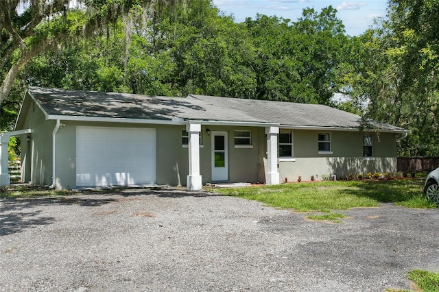 single story home featuring an attached garage, gravel driveway, and stucco siding