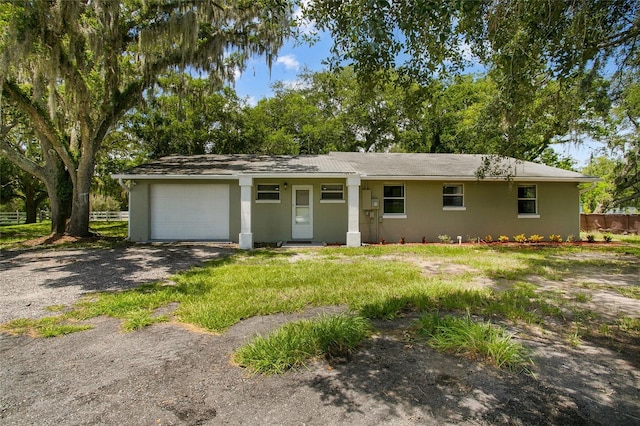 ranch-style home with an attached garage, fence, stucco siding, a front yard, and gravel driveway