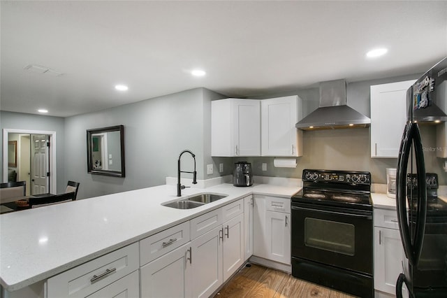 kitchen featuring a peninsula, a sink, white cabinetry, black appliances, and wall chimney exhaust hood