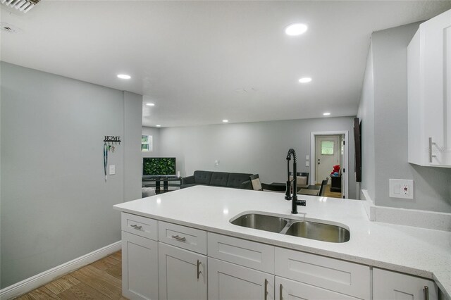 kitchen with light wood-style floors, white cabinets, a sink, and recessed lighting