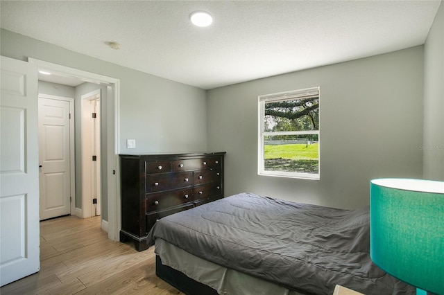 bedroom featuring baseboards, light wood-style flooring, and a textured ceiling