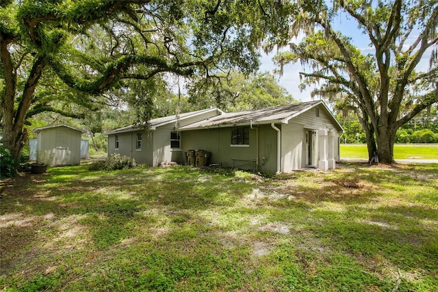 rear view of house featuring stucco siding, a lawn, an outdoor structure, and a storage unit