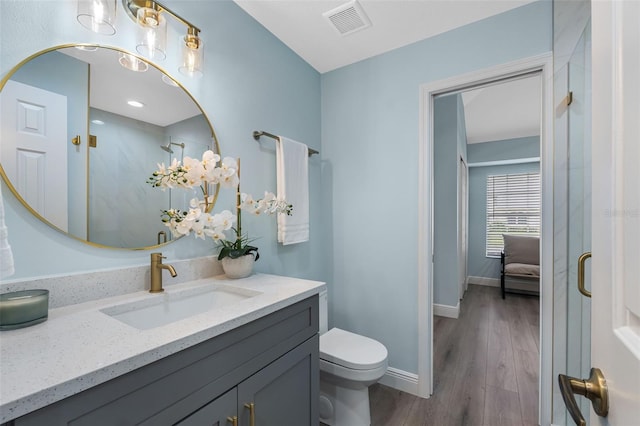 bathroom with toilet, hardwood / wood-style flooring, vanity, and walk in shower