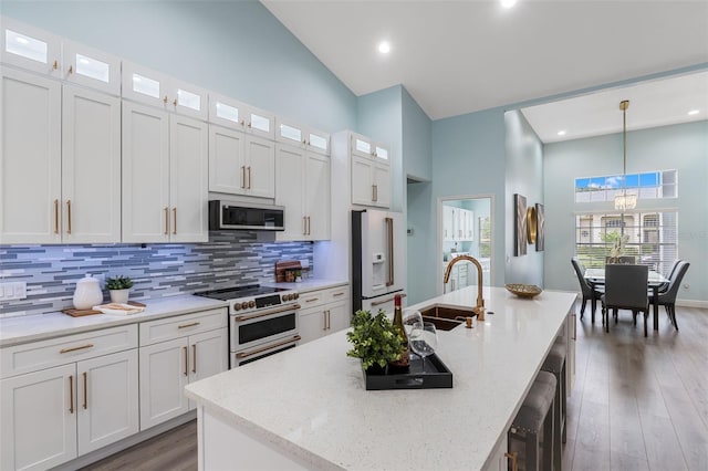 kitchen with high quality appliances, white cabinetry, hanging light fixtures, and an island with sink