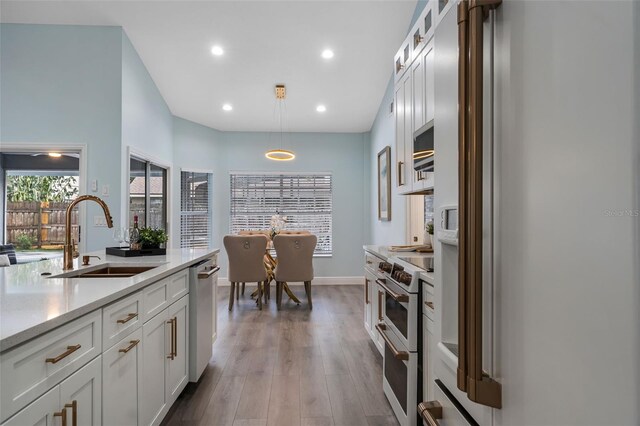 kitchen featuring white fridge with ice dispenser, light hardwood / wood-style flooring, sink, range with two ovens, and decorative light fixtures