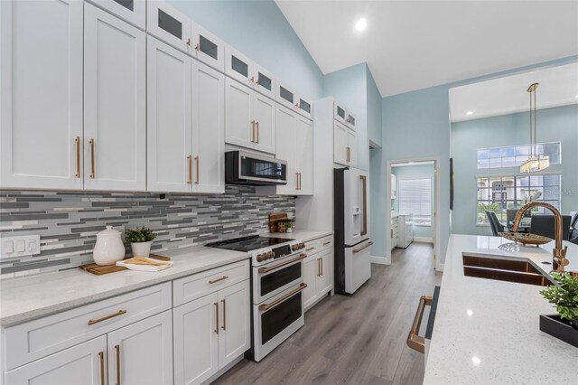 kitchen featuring white cabinetry, high quality appliances, decorative light fixtures, light wood-type flooring, and tasteful backsplash