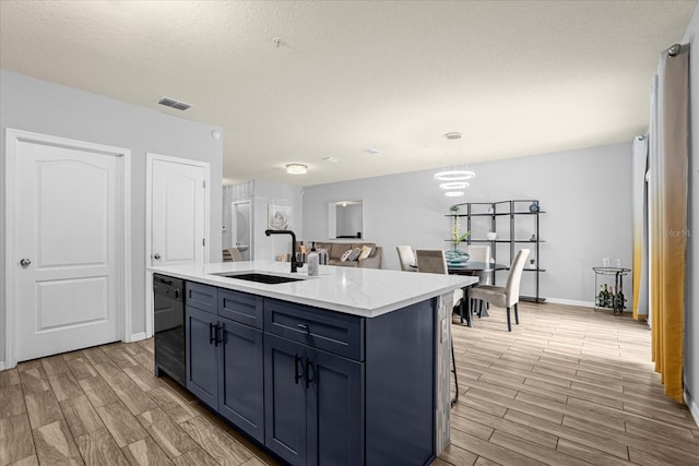 kitchen featuring sink, black dishwasher, decorative light fixtures, a center island with sink, and light wood-type flooring