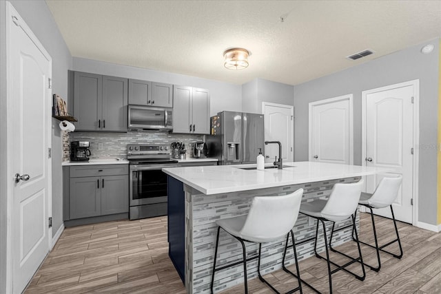 kitchen featuring gray cabinetry, sink, stainless steel appliances, a breakfast bar area, and a kitchen island with sink