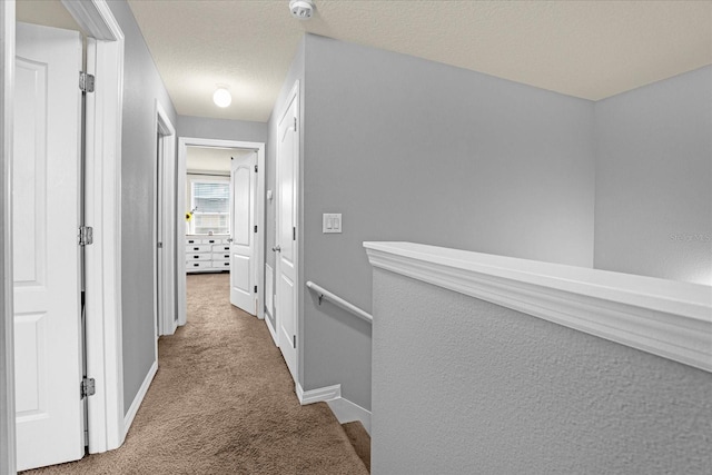 corridor with a textured ceiling, carpet, and baseboards