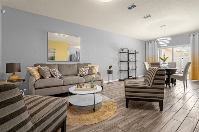 living room featuring a chandelier, visible vents, a textured ceiling, and wood finished floors