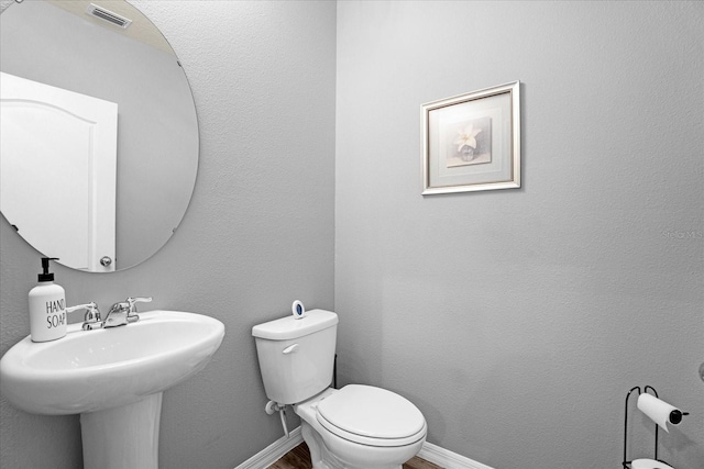 half bath featuring a textured wall, toilet, wood finished floors, visible vents, and baseboards